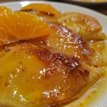 Detailed shot of Tender ao Molho de Laranja e Mel with droplets of orange sauce glistening.