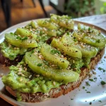 Aperitivo de torrada com abacate, decorada com queijo feta e ervas, em uma superfície de madeira.