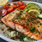 Prato de salmão grelhado com arroz, legumes frescos e molho de manteiga.