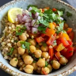 Uma tigela de grãos e legumes assados com grão-de-bico e vegetais frescos.