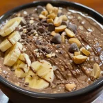 Close-up of a creamy bowl of chocolate peanut butter oatmeal topped with banana slices and chocolate chips.