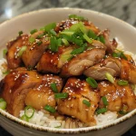 Close-up of juicy Frango Teriyaki in a bowl with sesame seeds and chopped green onions.
