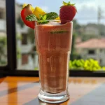 Close-up of a vibrant Smoothie de manga e morango in a glass, garnished with mint leaves.