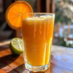 Close-up of a glass of Suco de Cenoura com Gengibre e Laranja, showcasing vibrant orange juice.