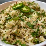 ['Close-up de arroz verde mexicano com pimentões e coentro.', 'Arroz verde servido em um prato, decorado com limão e pimentões.', 'Prato de arroz verde com ingredientes frescos ao lado.', 'Detalhe do arroz verde, mostrando a textura e cores vibrantes.']