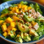 ['Salada de frango com manga e abacate em close.', 'Prato de salada colorida com frango, manga e abacate.', 'Detalhe da salada de frango, manga e abacate.', 'Salada fresca de frango, com pedaços de manga e abacate.']