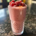 ['Close-up de um smoothie de framboesa cremoso em um copo.', 'Bebida de smoothie de framboesa com frutas e ingredientes frescos ao lado.', 'Vista lateral de um delicioso smoothie de framboesa em um copo transparente.', 'Imagem de um smoothie de framboesa decorado com framboesas frescas.']