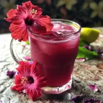 ['Copo de Chá de Hibisco Gelado com gelo e limão.', 'Bebida refrescante de Chá de Hibisco Gelado em close.', 'Vista lateral de um copo de Chá de Hibisco Gelado decorado.', 'Chá de Hibisco Gelado com rodelas de laranja e hortelã.']