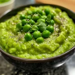 ['Purê de ervilhas verde e cremoso em um prato.', 'Close-up de purê de ervilhas com textura suave.', 'Purê de ervilhas servido em uma tigela.', 'Porção de purê de ervilhas com iluminação natural.']